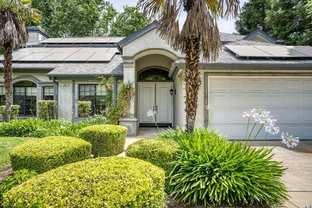 property entrance with a garage, roof mounted solar panels, and stucco siding