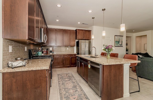 kitchen featuring stainless steel appliances, a sink, open floor plan, an island with sink, and decorative light fixtures