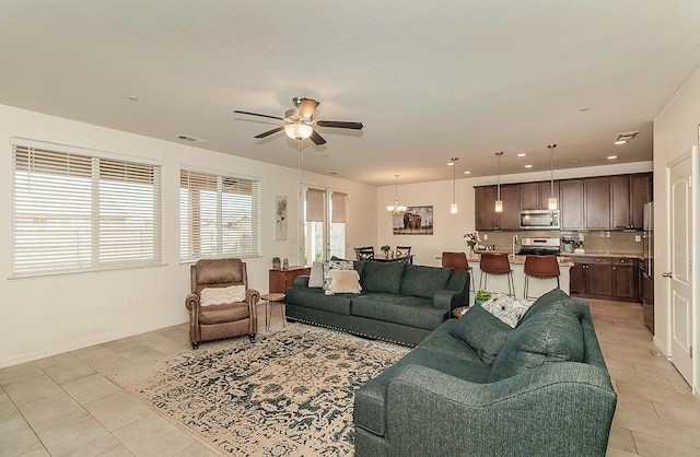 living room featuring light tile patterned floors, recessed lighting, ceiling fan with notable chandelier, visible vents, and baseboards