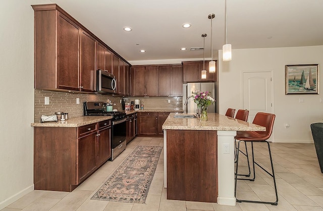 kitchen featuring light stone counters, a kitchen island with sink, stainless steel appliances, a kitchen bar, and decorative light fixtures