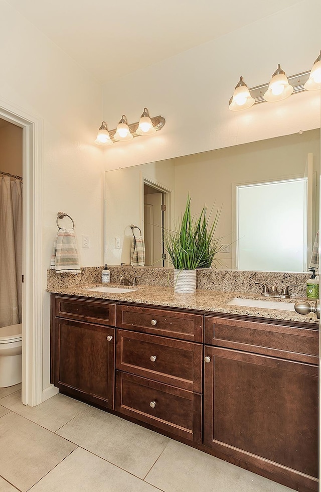 bathroom with toilet, double vanity, a sink, and tile patterned floors