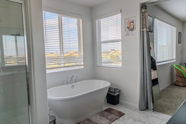 bathroom with a healthy amount of sunlight, a freestanding tub, baseboards, and marble finish floor