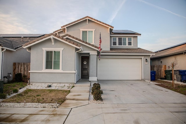 traditional-style home featuring an attached garage, solar panels, concrete driveway, a tiled roof, and stucco siding