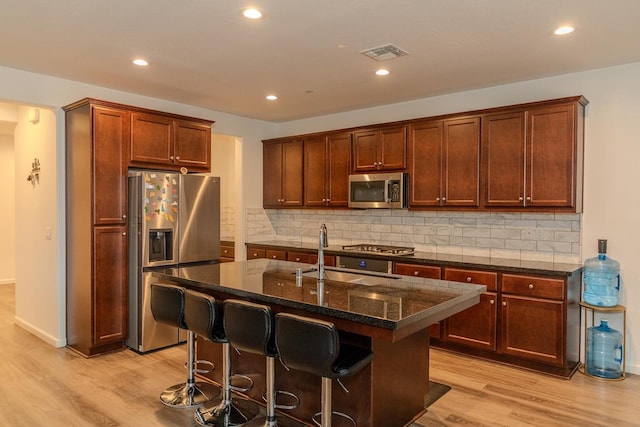 kitchen with a center island with sink, visible vents, dark stone counters, light wood-style flooring, and stainless steel appliances