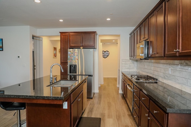 kitchen featuring stainless steel appliances, tasteful backsplash, a sink, and a center island with sink