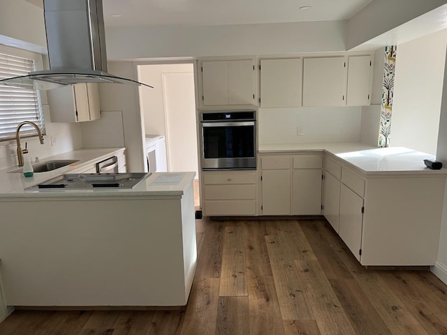 kitchen featuring island range hood, stainless steel appliances, a peninsula, a sink, and light countertops