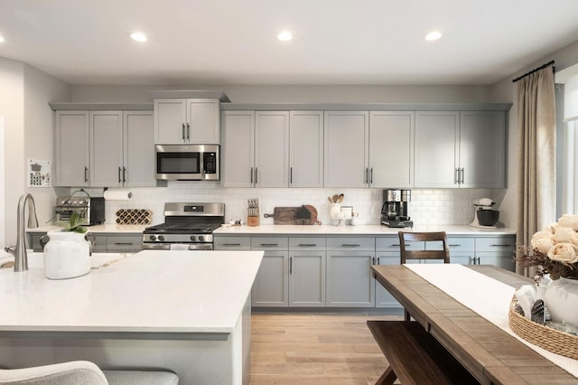 kitchen with tasteful backsplash, appliances with stainless steel finishes, light countertops, gray cabinetry, and light wood-style floors