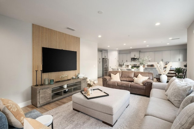 living room with light wood-style flooring, visible vents, baseboards, and recessed lighting