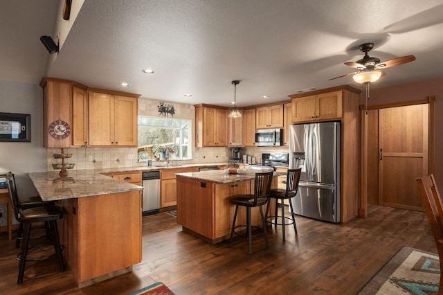 kitchen with hanging light fixtures, appliances with stainless steel finishes, a breakfast bar, and a center island