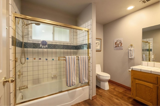 bathroom featuring bath / shower combo with glass door, visible vents, toilet, vanity, and wood finished floors