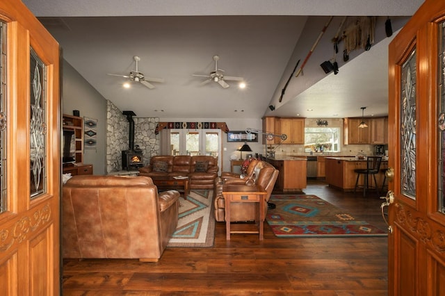 living area with lofted ceiling, dark wood-type flooring, a wood stove, and a ceiling fan