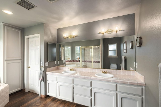 full bathroom featuring double vanity, a stall shower, visible vents, wood finished floors, and a sink