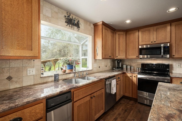 kitchen featuring appliances with stainless steel finishes, brown cabinetry, a sink, and light stone counters