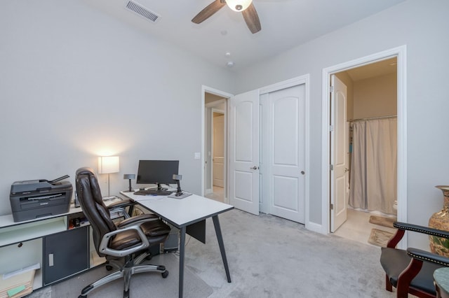 office space featuring a ceiling fan, visible vents, and light carpet