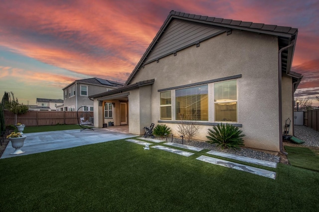 back of property at dusk featuring stucco siding, fence, a lawn, and a patio