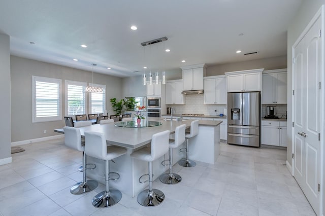 kitchen with stainless steel appliances, white cabinetry, light countertops, a center island with sink, and pendant lighting