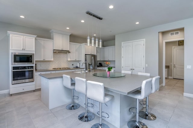 kitchen with light countertops, appliances with stainless steel finishes, a center island with sink, and white cabinets