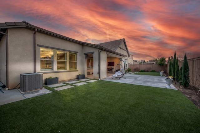 back of house at dusk with a patio, a fenced backyard, central AC, a lawn, and stucco siding