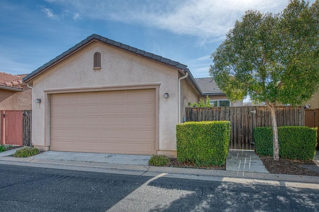 exterior space with an attached garage, fence, a tile roof, and stucco siding