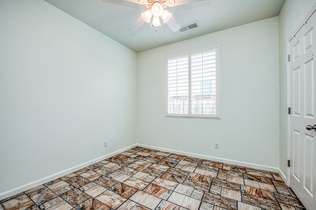 spare room featuring ceiling fan, stone finish floor, visible vents, and baseboards