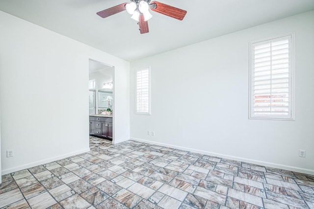 unfurnished room featuring ceiling fan, stone finish flooring, and baseboards