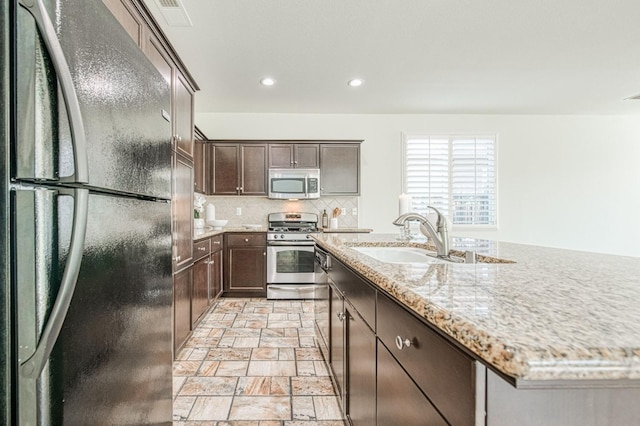 kitchen with stainless steel appliances, a sink, stone finish floor, decorative backsplash, and an island with sink