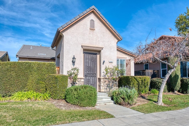 view of front of house with a front yard, stone siding, a tiled roof, and stucco siding