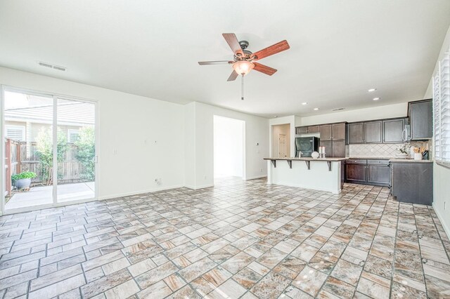 kitchen with visible vents, backsplash, open floor plan, an island with sink, and a kitchen bar