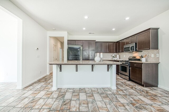 kitchen featuring a center island with sink, visible vents, appliances with stainless steel finishes, a kitchen breakfast bar, and backsplash