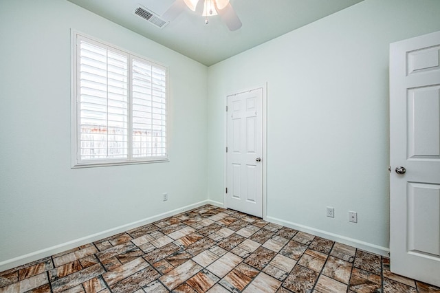 spare room featuring baseboards, visible vents, a ceiling fan, and stone finish flooring