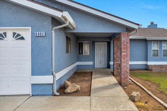 doorway to property featuring an attached garage and stucco siding