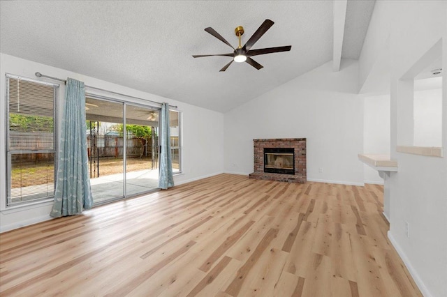 unfurnished living room featuring lofted ceiling, ceiling fan, a textured ceiling, a fireplace, and light wood finished floors