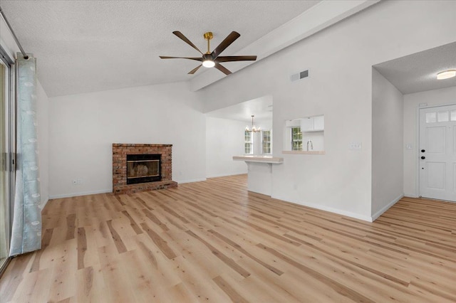 unfurnished living room with a textured ceiling, visible vents, vaulted ceiling, a brick fireplace, and light wood finished floors