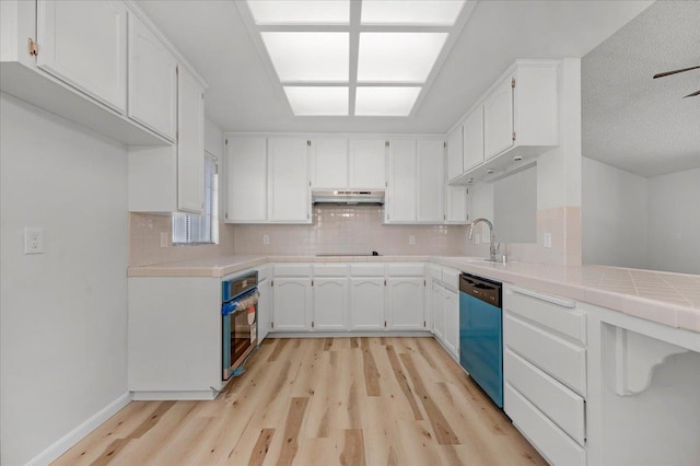 kitchen featuring tile countertops, dishwashing machine, oven, white cabinetry, and tasteful backsplash