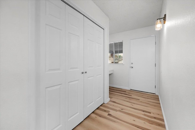 hallway featuring light wood-style floors, a textured ceiling, and baseboards