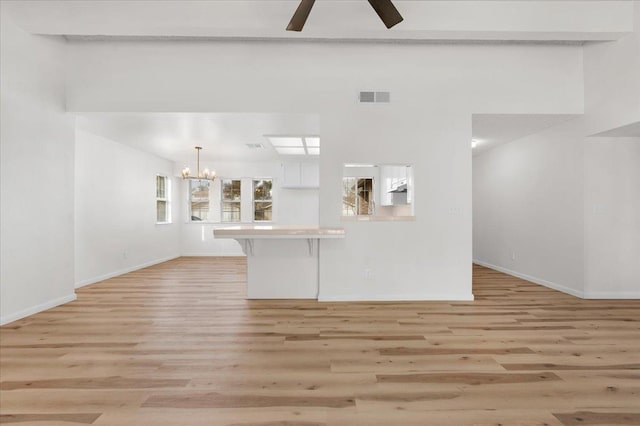 unfurnished living room featuring light wood-type flooring, baseboards, visible vents, and ceiling fan with notable chandelier