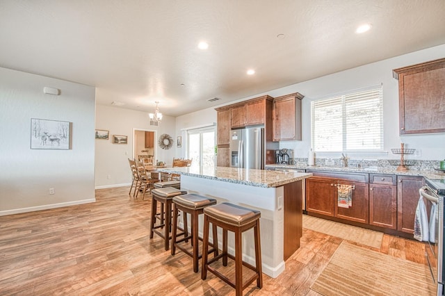 kitchen featuring a center island, a breakfast bar area, stainless steel appliances, light wood-style floors, and light stone countertops