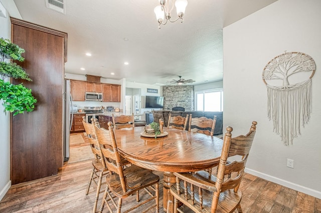 dining space featuring visible vents, light wood-style floors, a stone fireplace, a textured ceiling, and ceiling fan with notable chandelier