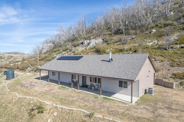 rear view of house featuring a shingled roof, cooling unit, roof mounted solar panels, and a patio