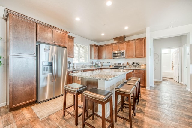 kitchen with light stone counters, stainless steel appliances, a center island, light wood finished floors, and a kitchen bar