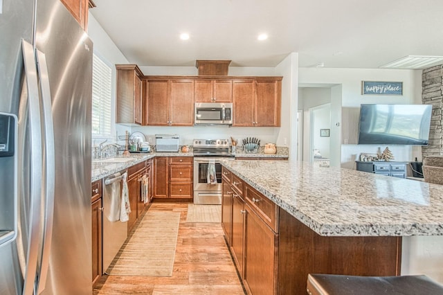 kitchen with light stone countertops, a sink, light wood-style floors, appliances with stainless steel finishes, and a center island