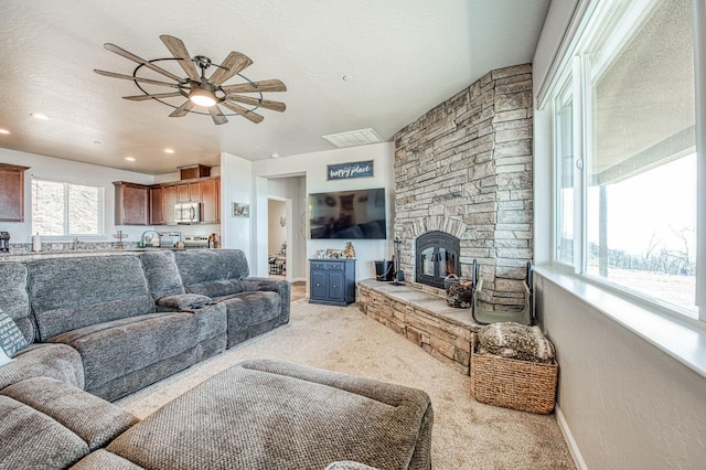 living room featuring baseboards, light colored carpet, ceiling fan, a textured ceiling, and a fireplace