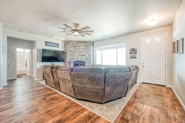 living area featuring visible vents, a ceiling fan, wood finished floors, a textured ceiling, and a fireplace