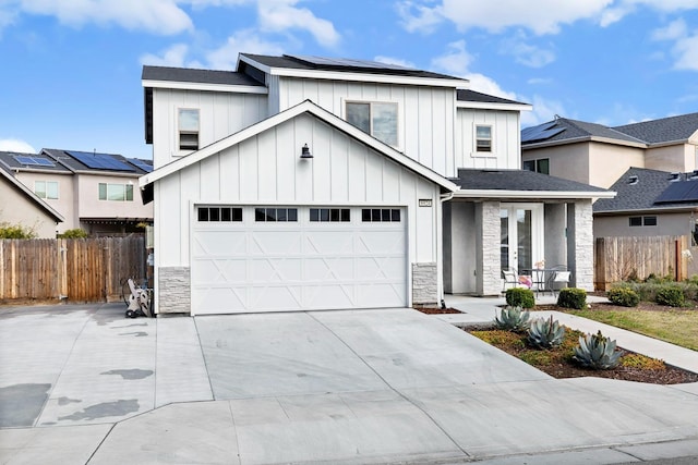 modern farmhouse style home with board and batten siding, roof mounted solar panels, fence, stone siding, and driveway