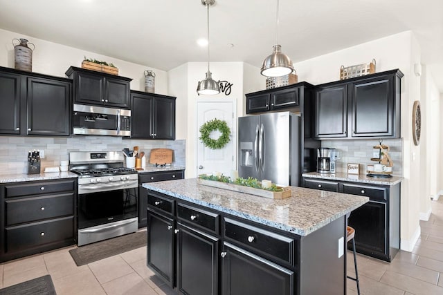 kitchen with appliances with stainless steel finishes, dark cabinetry, a kitchen island, and light tile patterned flooring