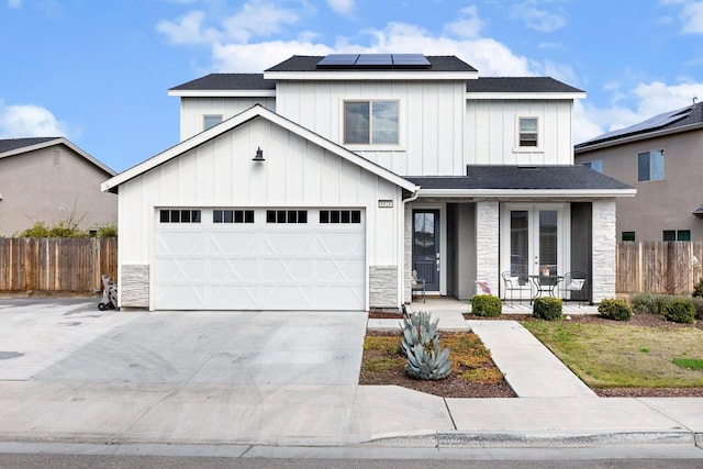 modern farmhouse style home featuring solar panels, fence, concrete driveway, french doors, and board and batten siding