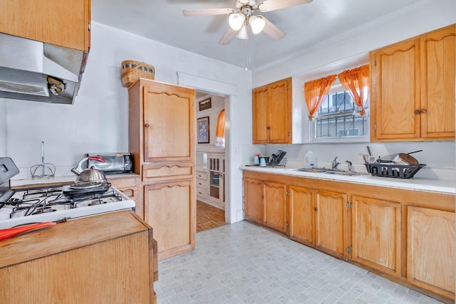 kitchen with ceiling fan, under cabinet range hood, a sink, light countertops, and gas range oven