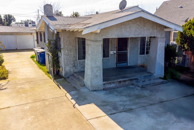 view of front facade with roof with shingles, a chimney, a patio area, and stucco siding