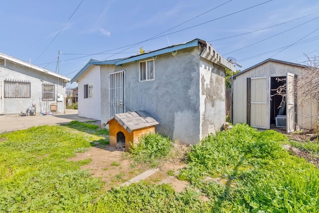 back of house with a storage shed, stucco siding, and an outbuilding