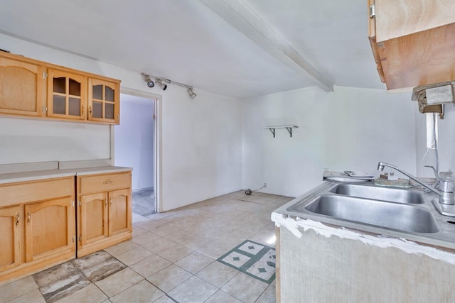 kitchen featuring light countertops, glass insert cabinets, light tile patterned flooring, a sink, and beamed ceiling